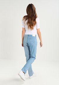 Jeans in denim blu chiaro con taglio dritto, dotati di una tasca posteriore e di un'etichetta sul cinturino, abbinati a sneakers bianche.