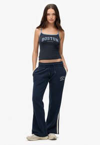 Marineblauwe crop top met de opdruk "BOSTON", gecombineerd met marineblauwe joggers met witte zijkanten en een trekkoord in de taille. Suède sneakers.