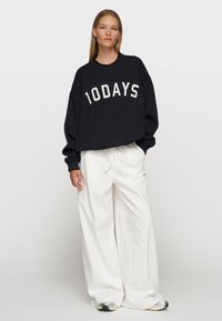 Schwarzes Sweatshirt mit dem Aufdruck "10DAYS" in Weiß, kombiniert mit locker sitzenden weißen Hosen. Das Outfit bietet einen entspannten Schnitt und weichen Stoff.