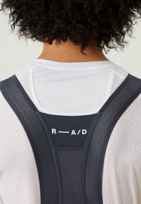 Juoda ir balta sportinė palaidinė su akių tekstūra ir plačiomis petnešomis. Ant nugaros yra prekių ženklo "R—A/D" logotipas, pabrėžiantis sportinį dizainą.