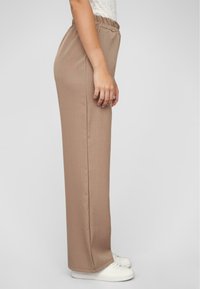 Beige, relaxed-fit broek met een elastische tailleband, zijnaad en rechte pijpen, gecombineerd met witte schoenen. Gladde textuur.