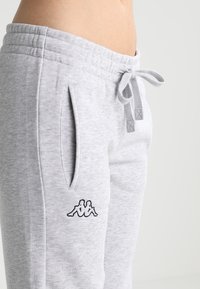 Gray sweatpants made of soft fabric, featuring an elastic waistband with a drawstring, side pockets, and a black logo on the left thigh.