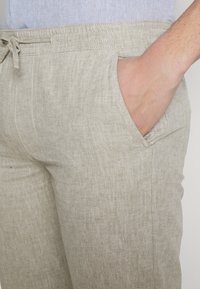 Beige linnebyxor med dragsko i midjan, sidofickor och en slät yta, som visar en enkel och ren design.