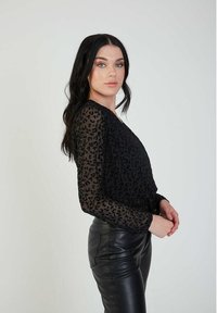 Black sheer top with long sleeves featuring a raised black leopard print pattern, paired with high-waisted black leather pants.