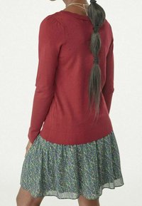 Červený pletený svetr s texturovanými puntíky na ramenou v kombinaci s květinovými zelenými šaty s vrstvenou sukní.