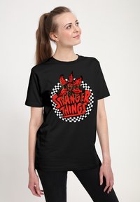 Czarny bawełniany t-shirt z czerwonym wzorem graficznym, na którym znajduje się napis "Stranger Things" oraz kratkowana ramka. Prosty fason z okrągłym dekoltem.