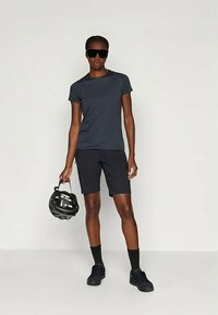 Tmavošedé atletické tričko s krátkymi rukávmi, v kombinácii s čiernymi šortkami a čiernymi teniskami. Nosenie slnečných okuliarov a drženie čiernej prilby.