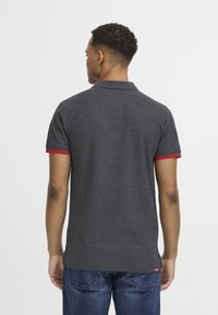 Mørkegrå polo shirt med røde kraveaccentuer, korte ærmer og lige kant. Stoffet ser let og let tekstureret ud.