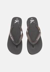 Sorte flip-flops med teksturert såle og doble svarte stropper. Har hvit "ck" logo og teksten "Calvin Klein Jeans". Designet for uformell bruk.