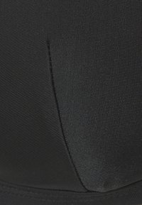 Sutien desportivo preto com tecido texturizado, costuras estruturadas e uma superfície suave. Apresenta um brilho subtil e detalhes cosidos ao longo das bordas.