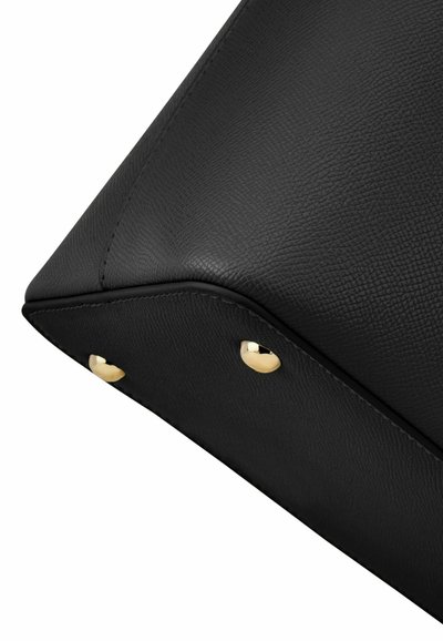 Črni ročno teksturirane usnjene torbice vogal z dvema zlata kovinska zaščitna zatiča na spodnjem robu.