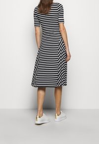 Black and white striped dress with a fitted bodice and flared skirt, paired with white sneakers featuring gold accents on the heel.