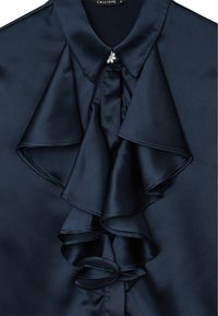 Navy blue satin blouse features a large, structured ruffle down the front, with a small pearl-like button at the collar. Smooth texture.