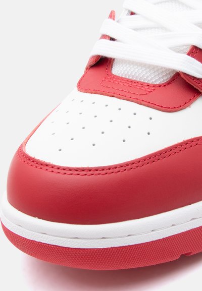 Κοντινό πλάνο από το μπροστινό μέρος ενός κόκκινου και λευκού αθλητικού παπουτσιού με διάτρητο λευκό δέρμα, λευκά κορδόνια, κόκκινες λεπτομέρειες και υφή στην κόκκινη άκρη της σόλας.