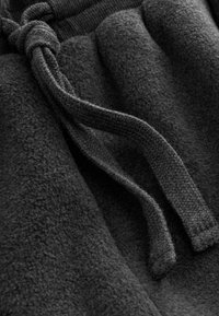 Mørkt fleece-stof med en blød tekstur, forsynet med en snoet snor i samme materiale, placeret på en lidt lysere baggrund.