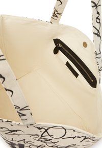 Bolso de lona con escritura abstracta negra sobre un exterior beige, que presenta un interior forrado y un bolsillo con cremallera con herrajes negros.