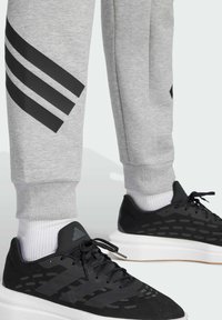 Gray sweatpants with three black stripes on the thigh, paired with black athletic shoes featuring a white sole and textured upper.