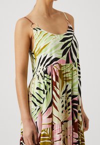 Ärmelloses Kleid mit einem mehrfarbigen tropischen Blättermuster in Grüntönen, Rosa und Braun, mit Metallringverzierungen an den Trägern.