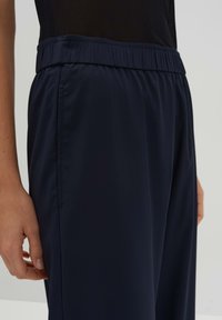 Marineblauwe sportbroek met een elastische tailleband en een soepele, lichte textuur. De zijnaden en de relaxte pasvorm bieden comfort.