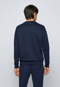 Mörkblå tröja med långa ärmar och rundad halsringning. Slät textur, ribbade ärmslut och nederkant, och ligger ovanför mörka byxor.