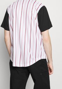 Camicia a maniche corte bianca e nera con strisce verticali rosse; morbido al tatto, vestibilità comoda e orlo arrotondato.