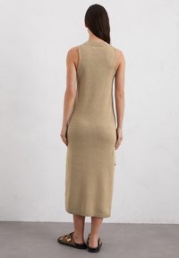 Robe sans manches en tricot de couleur beige clair, avec un col rond, design ajusté et longueur au genou, accompagnée de sandales marron à brides.