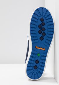 Baskets bleu marine avec une semelle en caoutchouc texturée bleue ornée d'un motif en losange et du logo Timberland orange. Une semelle intermédiaire blanche complète le design.