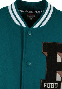 Tyrkysová vlněná varsity bunda s bílým pruhovaným žebrovaným límcem, zapínání na cvoky a velkým vyšívaným logem "FUBU" v kontrastních barvách.