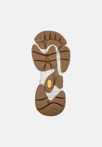 Podeszwa buta z brązowymi gumowymi wkładkami bieżnika, białą środkową podeszwą i żółtym logo Vibram na środku, rozmiar 38 widoczny w pobliżu pięty.