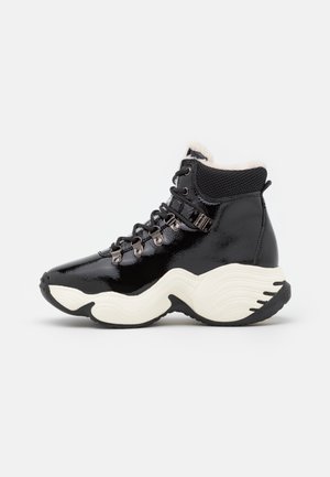 Zapatilla negra de caña alta con suela blanca gruesa y ondulada, ojales metálicos, cuello acolchado y forro de piel visible en el tobillo.