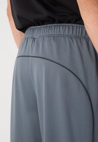 Pantalones deportivos grises con cinturilla elástica, que presentan una textura suave y un acento negro curvado a lo largo de la costura lateral.