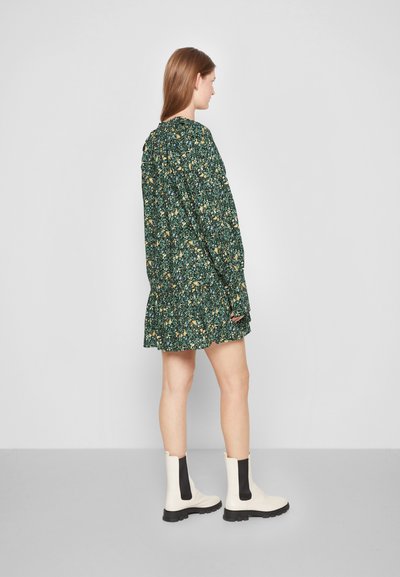Vestido floral verde com mangas longas, detalhes franzidos, barra com babados, combinado com botas em creme de tornozelo com painéis elásticos pretos.