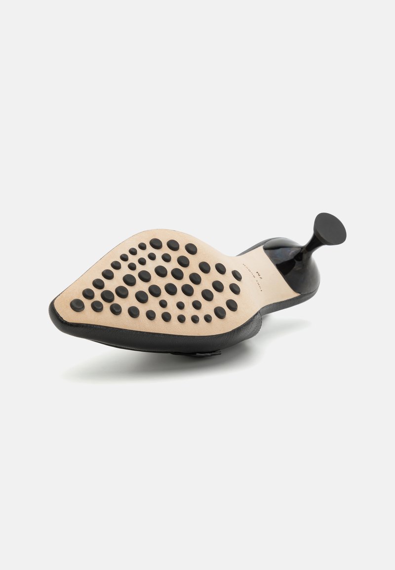 Escarpin noir à talon haut avec un bout pointu, présentant une semelle en caoutchouc texturé et un motif circulaire sur la partie inférieure.