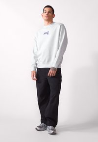 Felpa grigia con la scritta "NYC 93" stampata in blu, pantaloni cargo neri e sneakers grigie con dettagli argentati. Look casual e vestibilità rilassata.