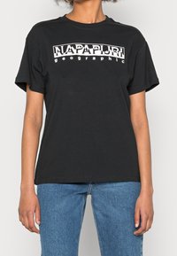 Sort t-shirt lavet af bomuld med et stort hvidt "NAPAPIJRI geographic" grafisk tryk over brystet, rund hals og korte ærmer.