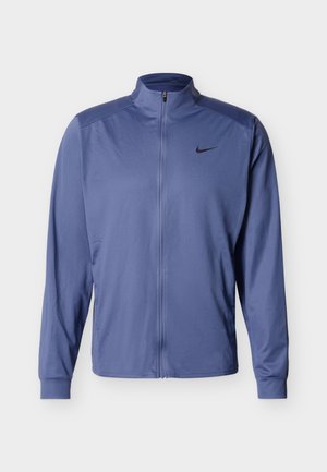 Μπλε μπουφάν Nike με πλήρη φερμουάρ και μακριά μανίκια, με μαύρο λογότυπο Nike στο αριστερό στήθος, στέκεται μπροστά σε απλό λευκό φόντο.