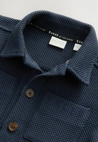 Marineblauw polo-shirt met een gestructureerd, wafelontwerp, een omgevouwen kraag en twee bruine knopen. Voorzien van een geborduurd "BAKER"-logo.