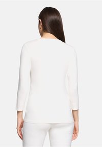 Weißes langärmeliges Oberteil mit rundem Halsausschnitt, glatter Textur und taillierter Form, von hinten betrachtet. Kombiniert mit passenden weißen Hosen.