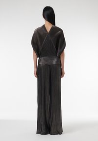 Metallisch schwarzes Outfit mit einer strukturierten, plissierten weit geschnittenen Hose und einem locker geschnittenen Oberteil mit V-förmig ausgeschnittenem Rücken. Ein subtiler Glanz verstärkt das Design.