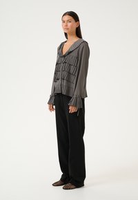 Top grigio con pieghe e scollatura a V, arricchito da volant sovrapposti e maniche a campana, abbinato a pantaloni neri a vestibilità comoda e scarpe nere con texture.