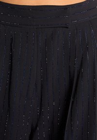 Zwarte broek met een brede tailleband, voorzien van verticale blauwe en zilveren strepen en een zachte textuur.