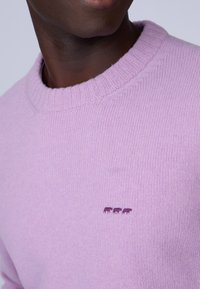 Pull en maille violet clair avec un col côtelé et un petit détail brodé de trois vaches d'un violet plus foncé sur la poitrine.