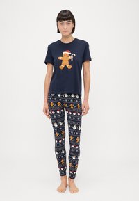 Camiseta navy con un hombre de jengibre sosteniendo un bastón de caramelo, combinada con leggings estampados que muestran motivos navideños en varios colores.