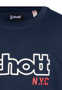 T-shirt en coton bleu marine avec un grand logo blanc agrémenté d'accents rouges affichant "Schott N.Y.C.". Modèle à col rond avec des manches courtes.
