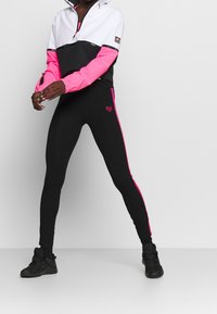 Svart och rosa träningsoutfit med en färgblockerande jacka med halvdragkedja och eleganta svarta leggings med rosa sidband och logodetalj.