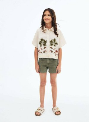 Kortärmad krämfärgad skjorta med grön och brun blommönstring, matchad med olivgröna shorts och beigea slidesandaler.