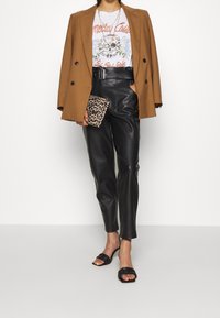 Brun dubbelknäppt kavaj, vit t-shirt med grafisk design, svarta läderbyxor, leopardmönstrad clutch, svarta flätade slide-sandaler.