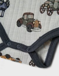 Bērnu bodijs ar tumšu apdari un pieliekamām pogām, uz mīksta, ribotā balta auduma, kuru rotā vintage automobiļu ilustrācijas.