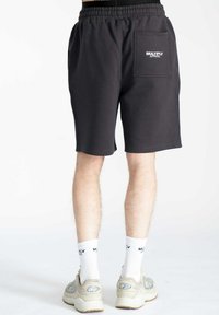 Pantaloni corti neri realizzati in un tessuto texturizzato, dotati di una cintura elastica e una tasca posteriore con il logo bianco "MULTIPLY APPAREL".