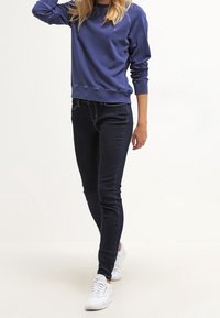 Tijdloze donkerblauwe jeans met een soepele textuur en subtiele stikdetails, gecombineerd met een effen, lange mouwen, ronde hals sweatshirt.